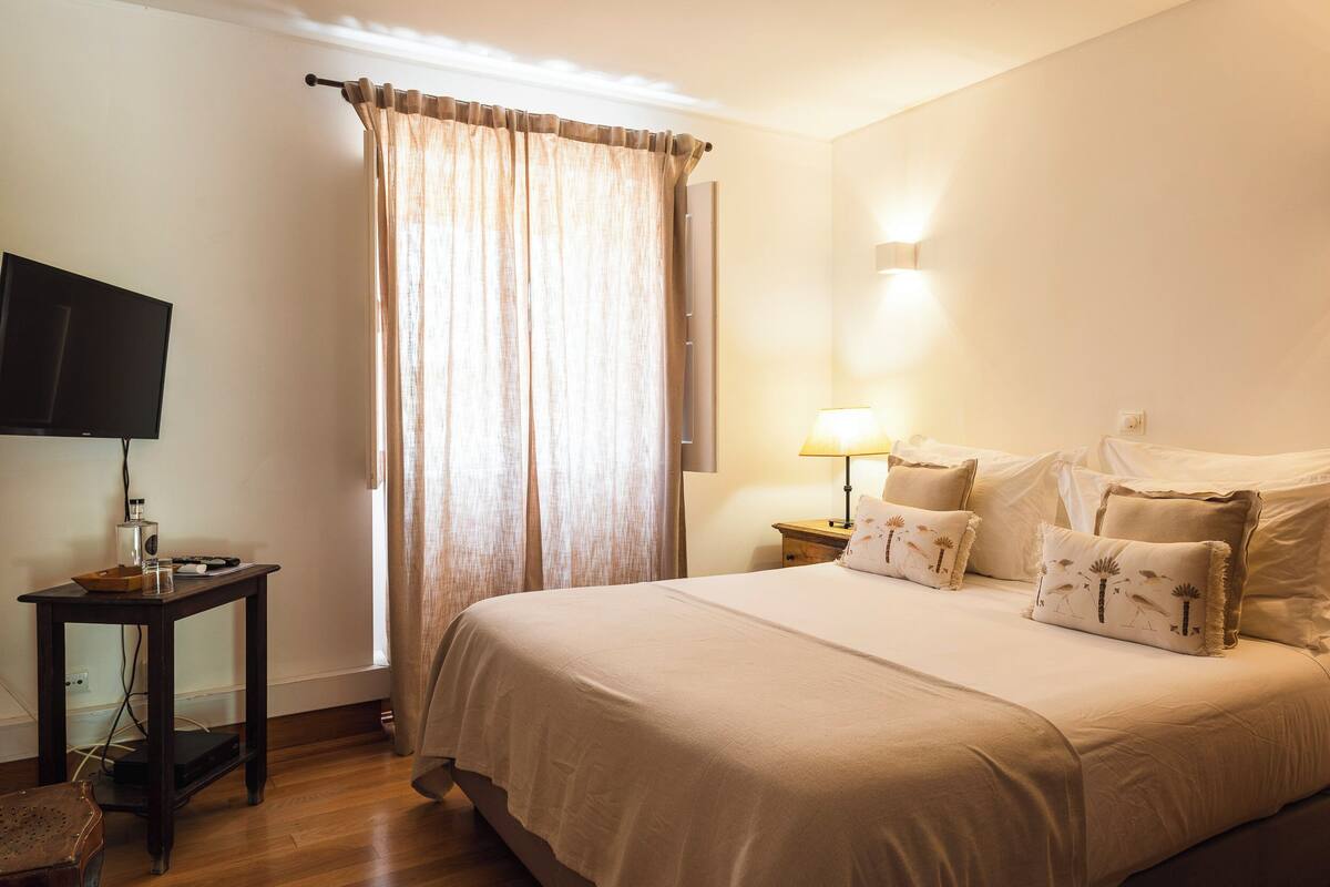 Une chambre à coucher avec un lit, une télévision, une lampe et une fenêtre avec des rideaux.