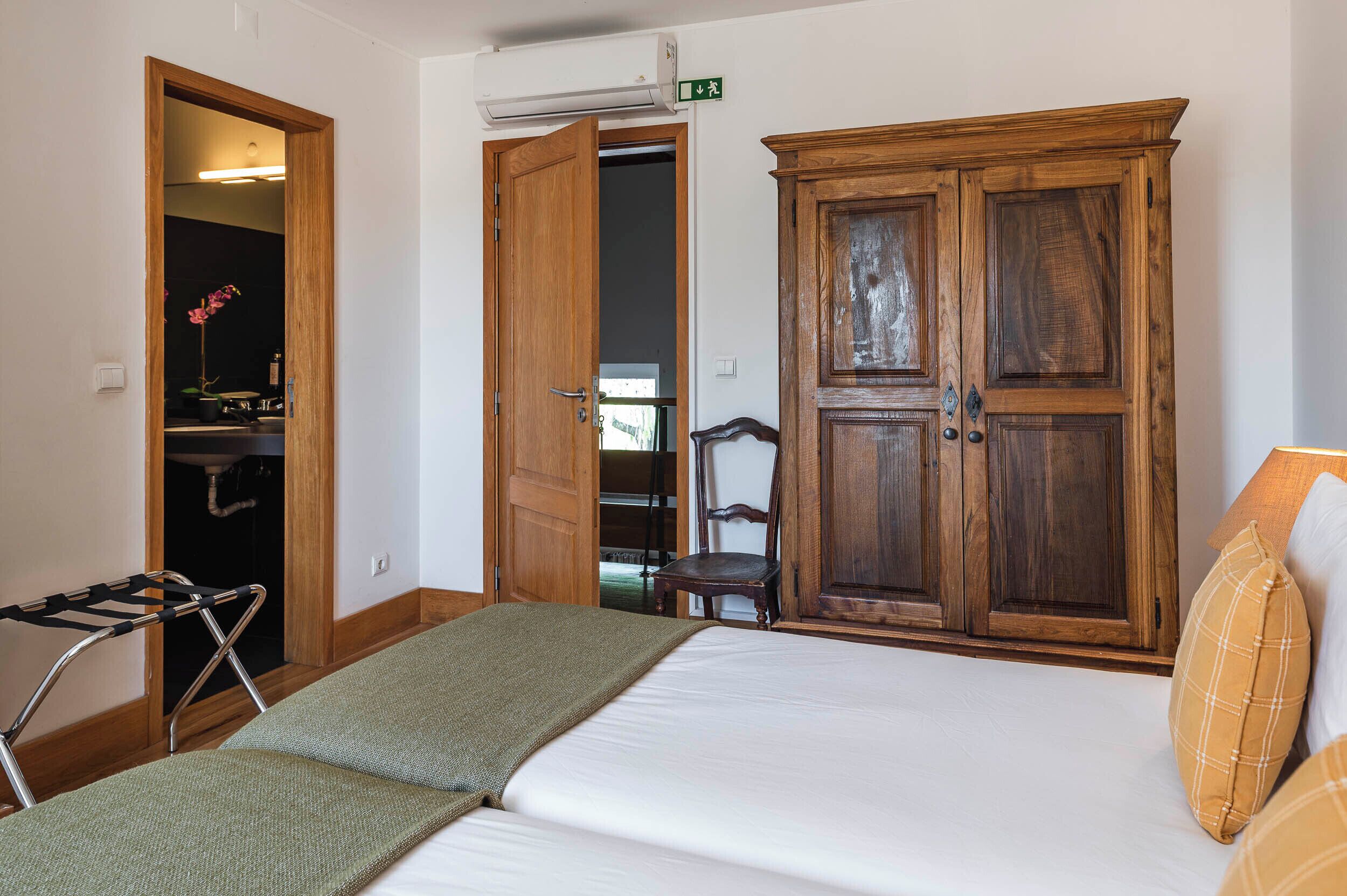 Une pièce comprenant un lit, une armoire en bois, une chaise et un étendoir.