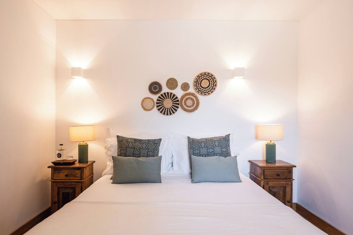 Une chambre à coucher bien rangée, avec un grand lit, deux tables de chevet et des lampes fixées au mur.