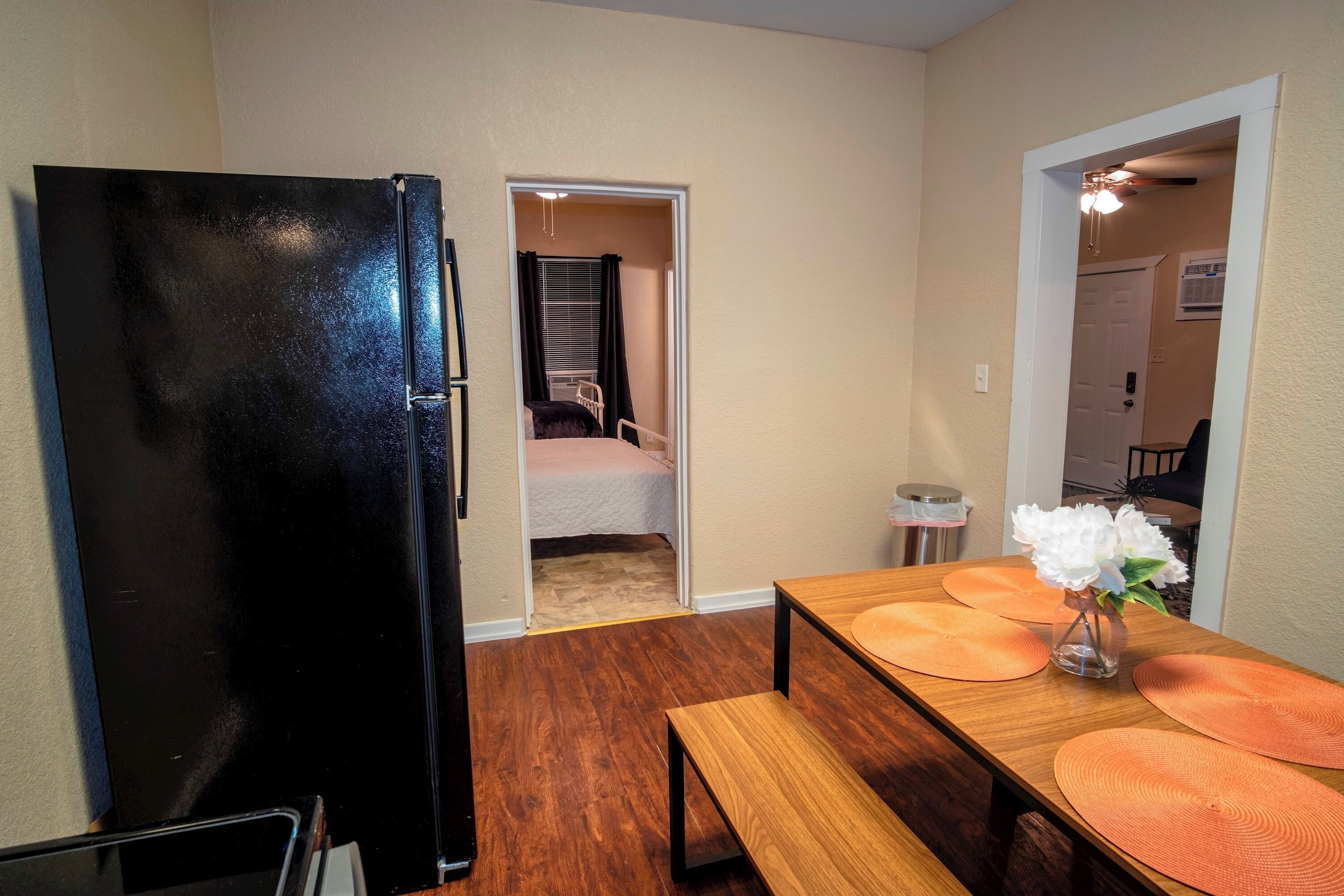 A compact kitchen with a black refrigerator, wooden dining table with orange placemats, and a bench.