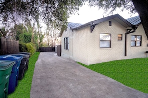 A single-story house with a brick exterior, a concrete driveway, and a fenced yard. - Cozy Downtown Guest House 2br/1ba Sleeps 8 (San Antonio)