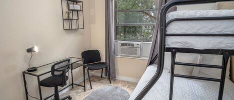 A compact room with a bunk bed, a desk with a chair, a small rug, and a window with curtains.