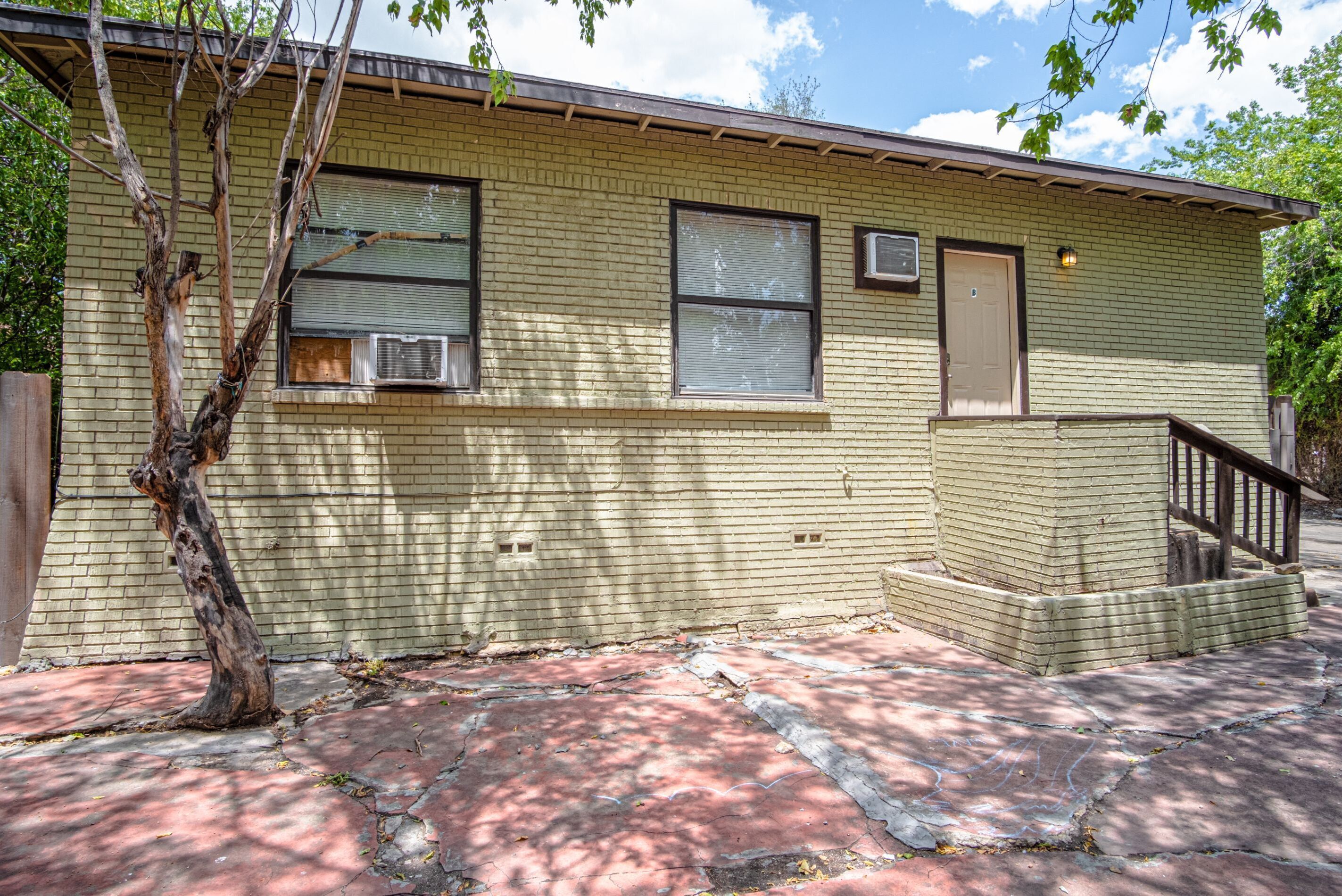 A small brick building with two windows, a door, and a small staircase leading to a porch.