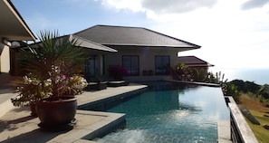 A modern house with a swimming pool, potted plants, and a view of the ocean.