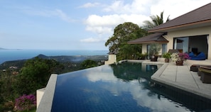 A modern house with a swimming pool overlooking a scenic view of the ocean and hills.