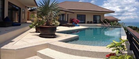 A modern house with a swimming pool, outdoor seating, and a view of the ocean.