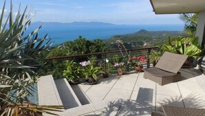 A balcony with a view of the ocean, potted plants, and a wicker chair.