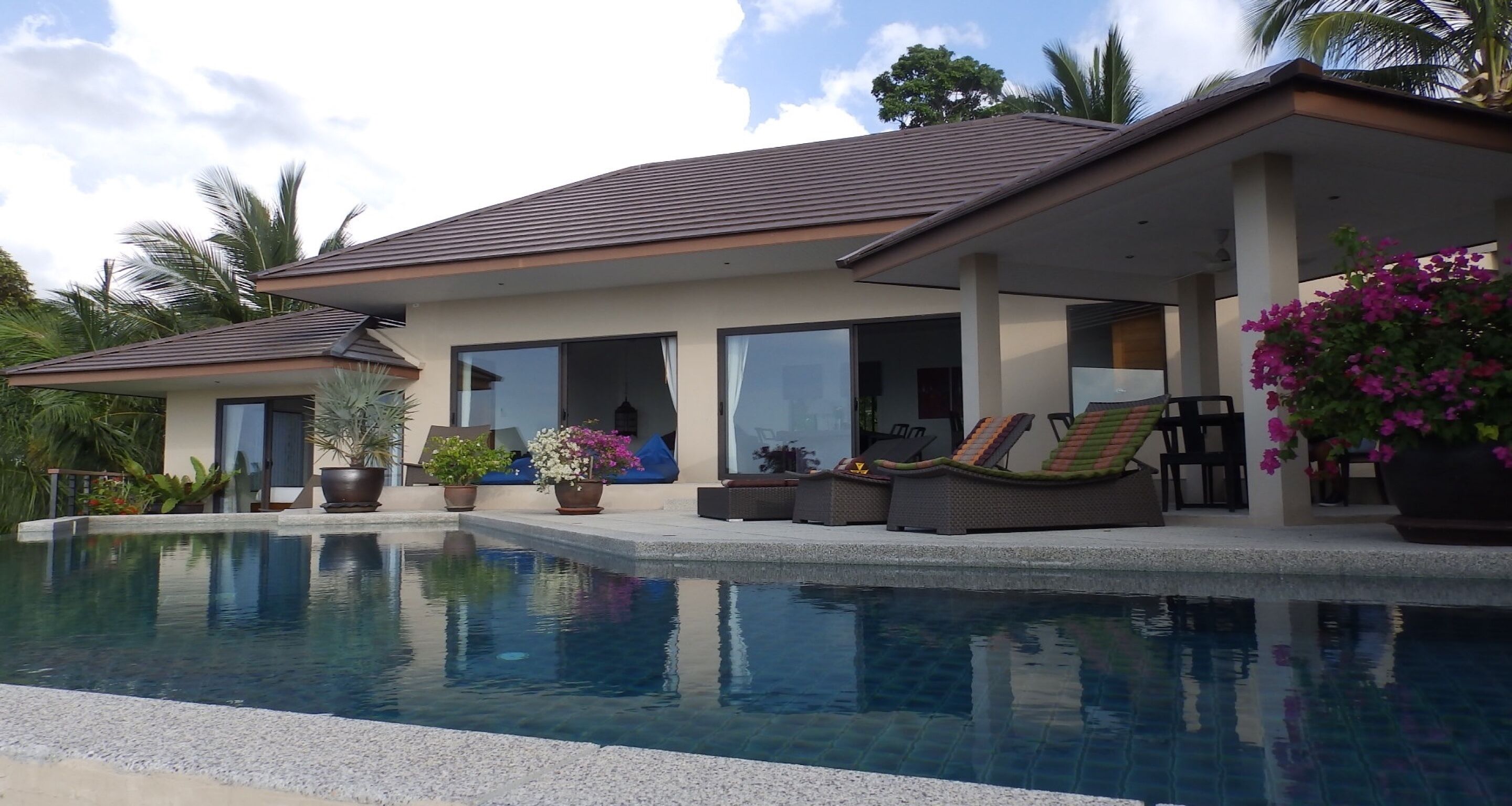 Una casa moderna con piscina, mobiliario de exterior y plantas en macetas.