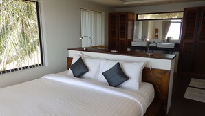 A hotel room with a bed, a wooden headboard, a vanity with a mirror, and a window with blinds.