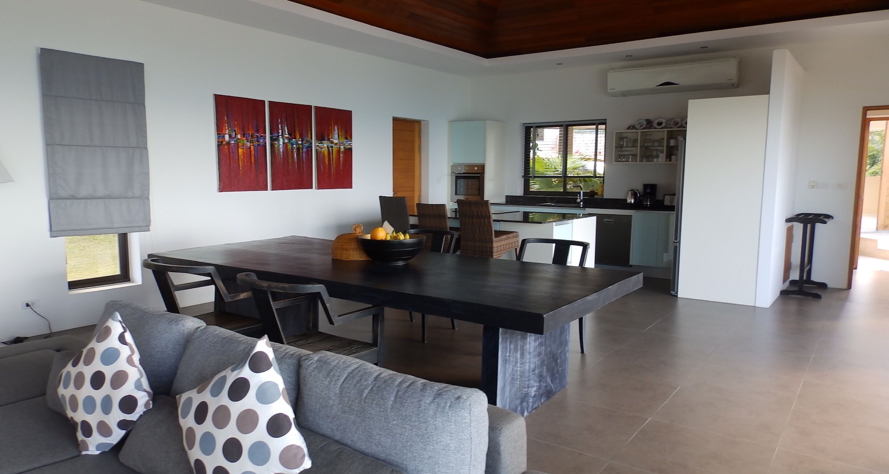A modern living room with a dining area, a kitchen, and a view of the outdoors.