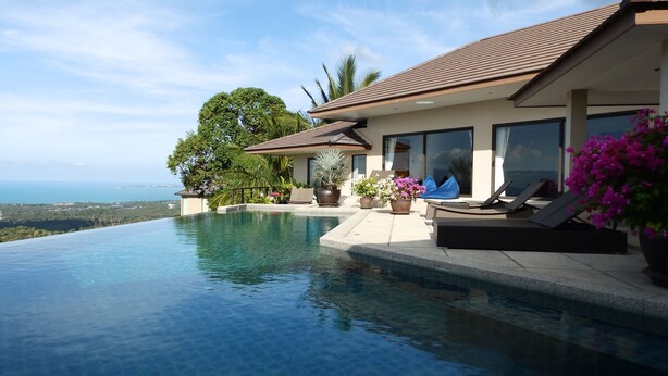 A modern house with a large infinity pool, a patio with lounge chairs, and a view of the ocean.