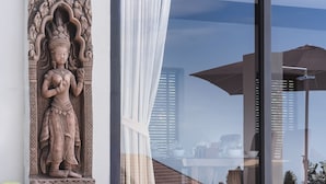 Uma estátua na parede, uma porta de vidro com cortina e vista para edifícios.