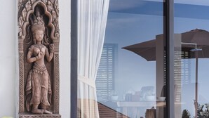 A statue on a wall, a glass door with a curtain, and a view of buildings. - 2 Bedroom Sea View Villa Bubbles (Koh Samui)