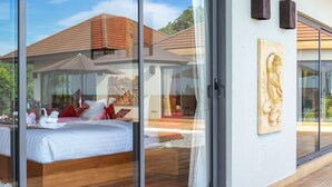 Een moderne slaapkamer met een groot bed, uitzicht op een zwembad en een tropisch landschap.