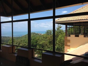A room with large windows offering a view of a coastal landscape and a building with a tiled roof.