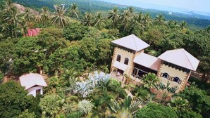 Um edifício grande, com dois andares, cercado por vegetação exuberante e palmeiras.