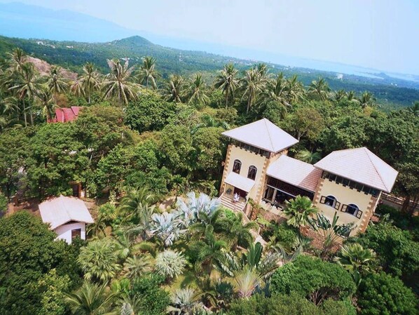 A large, two-story building surrounded by lush greenery and palm trees.