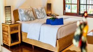 Une chambre à coucher avec un lit en osier, du linge de lit blanc et deux lampes de chevet.