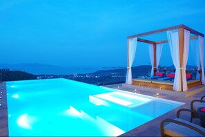 Zona de piscina con un toldo y asientos, con vistas a un paisaje urbano.