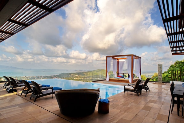 A pool area with lounge chairs and a canopy overlooking a scenic landscape.