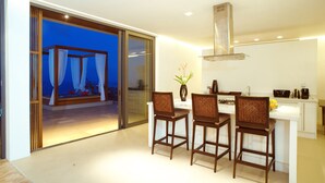 A modern kitchen with a dining area, featuring a large island, bar stools, and a sliding glass door leading to a balcony with a view. - 2 Bedroom Sea View Villa Blue SDV080H-By Samui Dream Villas (Koh Samui)