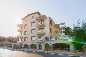 A multi-story hotel with balconies, a covered entrance, and potted plants.