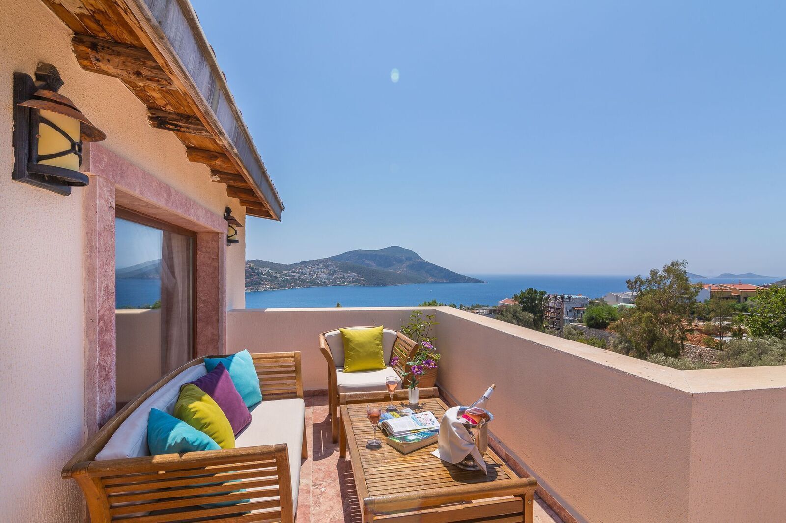 Ein Balkon mit Holztisch, Stühlen und Kissen, mit Blick auf die Küste, Berge und das Meer.