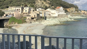 Un village côtier avec des bâtiments qui bordent le rivage, une plage rocheuse et une vue dégagée sur la mer.
