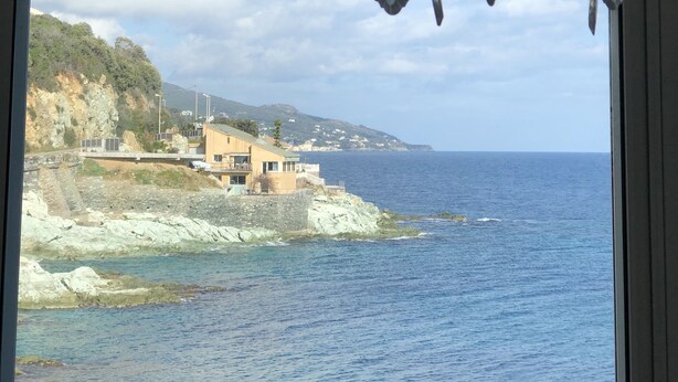 Une pièce offrant une vue sur un paysage côtier, comprenant un bâtiment situé sur une côte rocheuse et la mer.