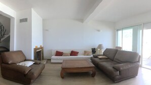 Un salon avec deux canapés marron, un canapé blanc et une table basse en bois. On y trouve une cheminée sur laquelle sont posées deux bougies.