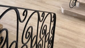 Une pièce avec un plancher en bois, un canapé blanc orné d’un coussin rouge, une petite table ronde avec une lampe, et une rambarde en métal noir.