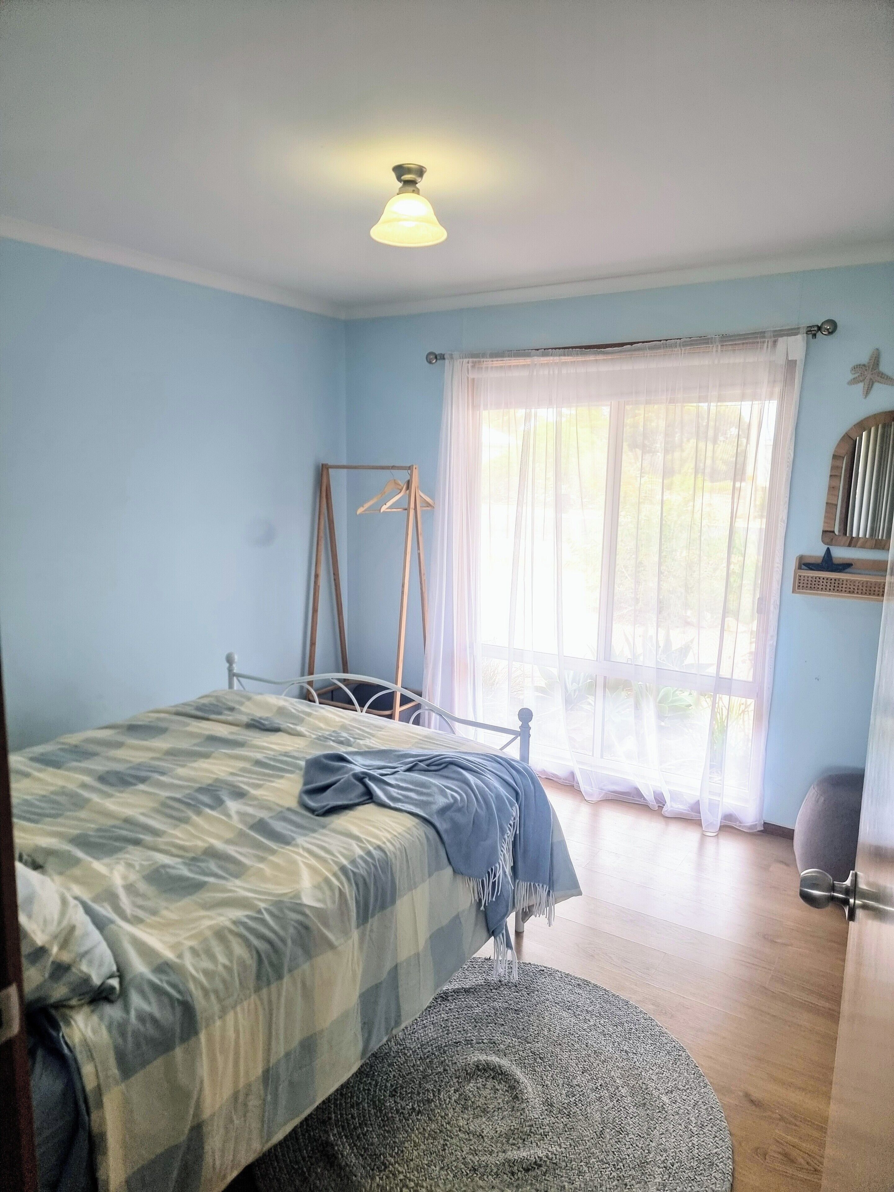 A bedroom with a bed, a hanging chair, a window with sheer curtains, and a starfish decoration on the wall.