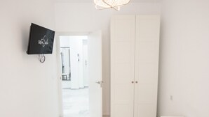 Una habitación de hotel con un armario blanco, un televisor de pantalla plana montado en la pared y una mesita de noche con un control remoto.