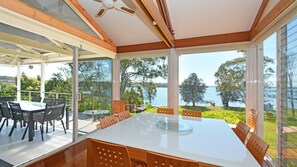 Enjoy meals at the large dining table surrounded by comfortable chairs, with expansive views of the lake and greenery.
