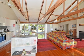 Ein geräumiges Wohnzimmer mit Holzboden, eine Küche mit modernen Geräten und ein farbenfrohes Sofa.