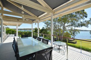 Un espace extérieur abrité, aménagé pour prendre les repas, avec une table et des chaises en verre, donnant sur un lac.