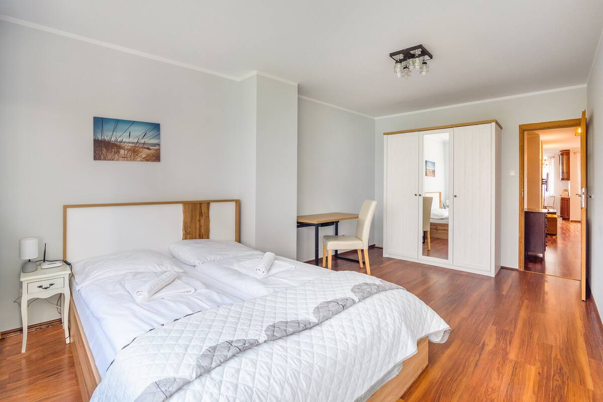 A bedroom with a bed, bedside table, chair, and a desk with a chair.
