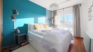 Ein modernes Schlafzimmer mit Bett, Nachttischlampen, einem Fenster mit Vorhängen und Blick auf die Stadt.
