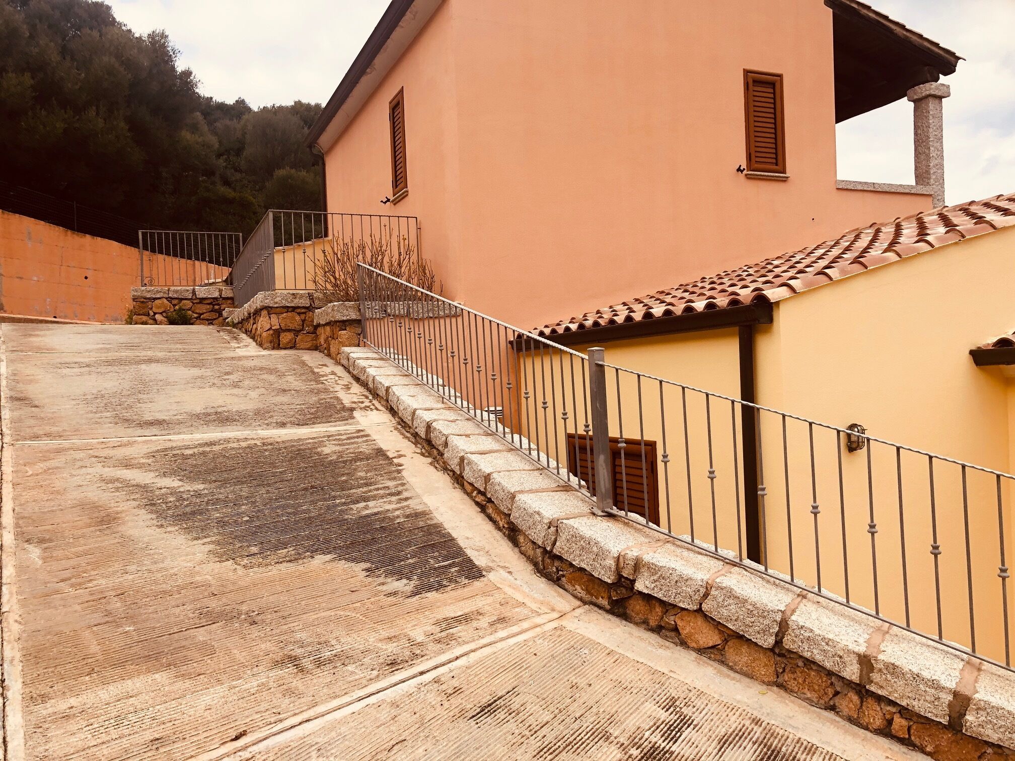 A building with a stone wall and metal railing, a tiled roof, and a stone staircase leading up.