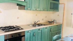 A kitchen with teal cabinets, a gas stove, a sink, and a table with a sunflower tablecloth. - Fantastico San Teodoro STRAU02 (San Teodoro)