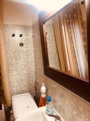 A bathroom with a tiled wall, a mirror, a sink, and a bottle of hand soap.