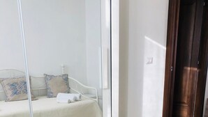 A bedroom with a bed, a chair, a mirror, and a wooden door.
