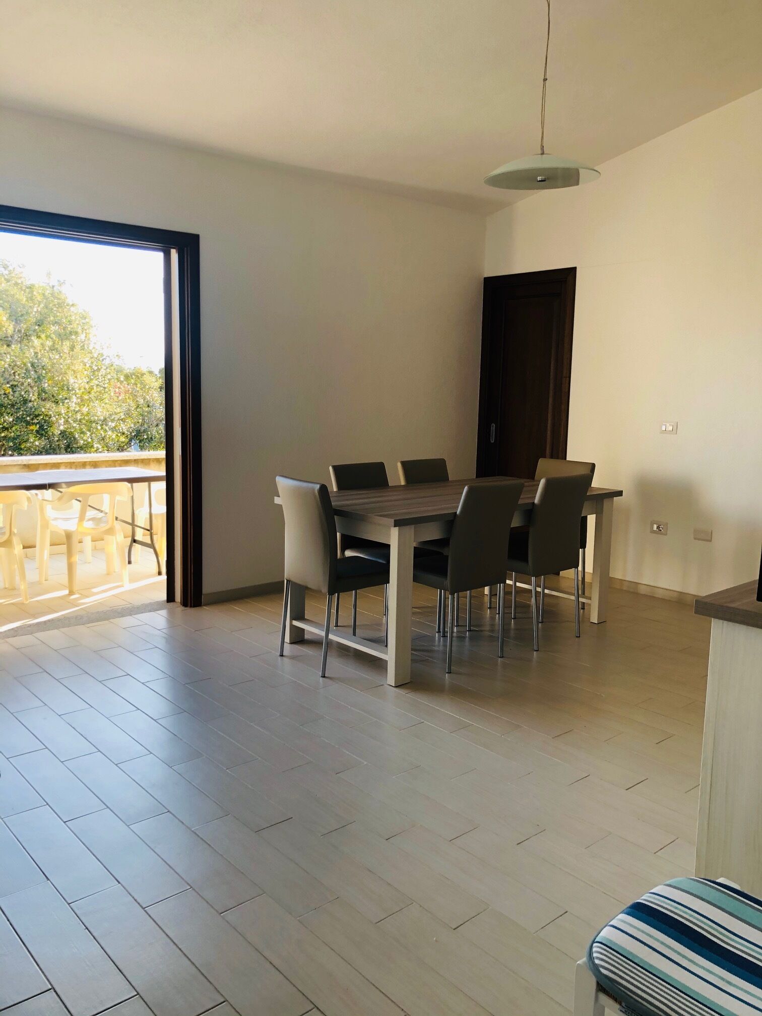 A dining area with a table and chairs, a sliding glass door leading to a balcony, and a light fixture above.