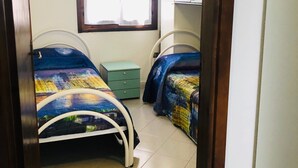 A bedroom with two beds, a window, a green nightstand, and a white wardrobe.