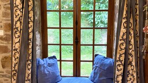 Ein Zimmer mit Stehwänden, einem großen Fenster, einer eingebauten Bank mit Kissen und Vorhängen.