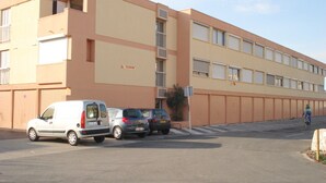 Un edificio con fachada plana, varias ventanas y un estacionamiento con varios coches.