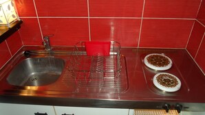 Una cocina con un lavamanos de acero inoxidable, un escurreplatos rojo y dos platos blancos con un diseño marrón.