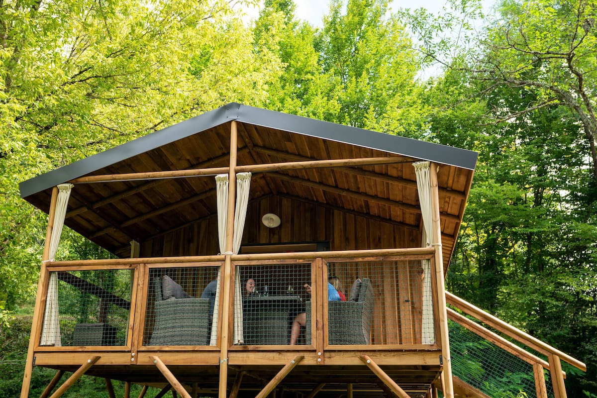 A wooden cabin with a balcony, surrounded by trees.