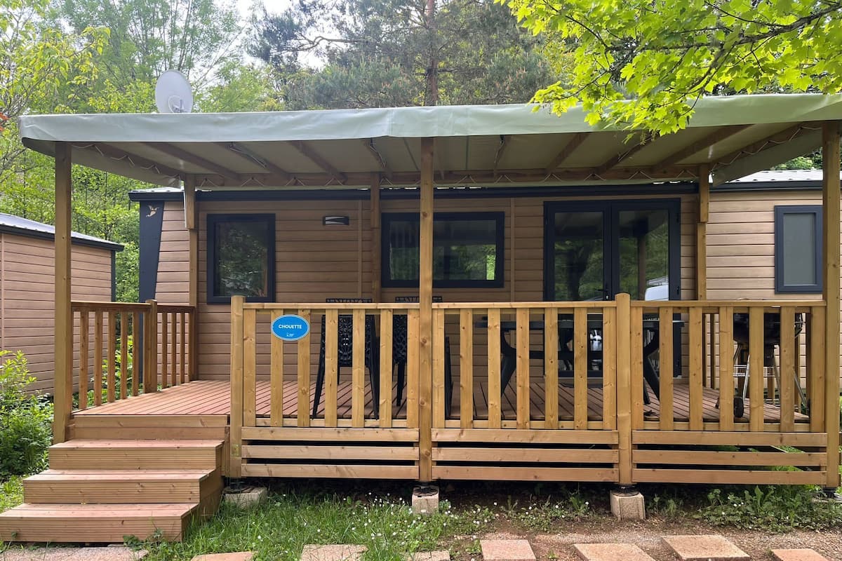 A wooden cabin with a covered deck, a satellite dish, and a sign indicating the name 'Chouette'.