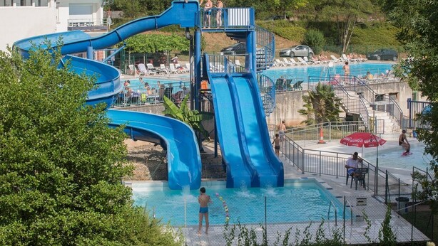 A water park with a large blue water slide, a swimming pool, and lounge chairs. - Camping Collonges-la-Rouge (Collonges-la-Rouge)